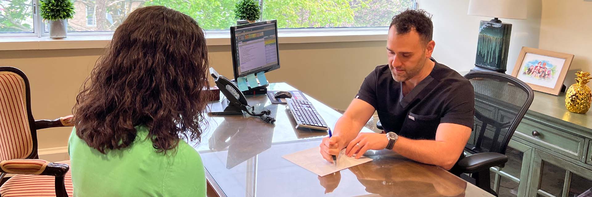 Dr. Barry Perlman seated at desk across from a patient. With pen and paper he illustrates a procedure.